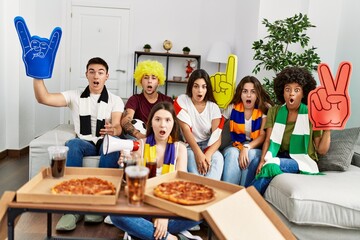 Group of young people wearing team scarf cheering football game scared and amazed with open mouth for surprise, disbelief face