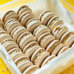 Fresh white macaroons with coconut in box on yellow background