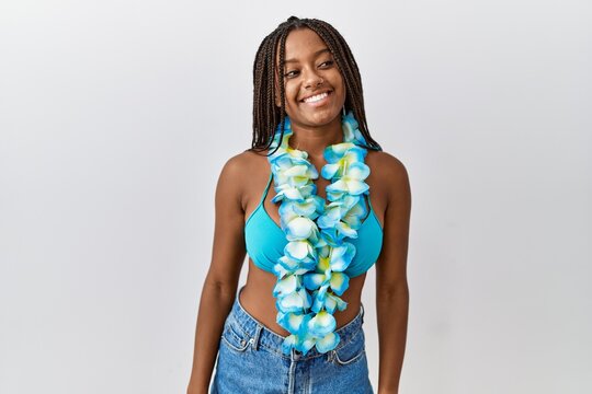 Young african american woman with braids wearing bikini and hawaiian lei looking away to side with smile on face, natural expression. laughing confident.
