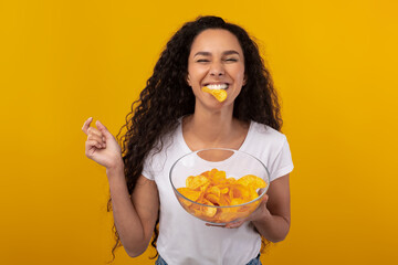Excited Latin Lady Eating Delicious Potato Crisps - obrazy, fototapety, plakaty