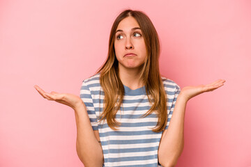 Young caucasian woman isolated on pink background confused and doubtful shrugging shoulders to hold a copy space.