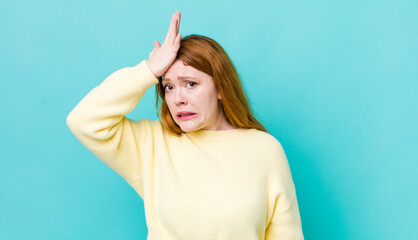 pretty red head woman raising palm to forehead thinking oops, after making a stupid mistake or...