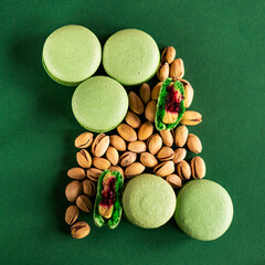 Delicious green macaroons with berry filling and pistachios lie on a green background. Sweet food and desserts.