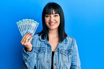 Young hispanic woman holding bangladesh taka banknotes looking positive and happy standing and...