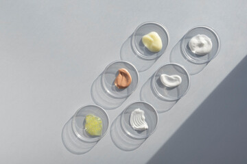 Multicolored textures of cream, scrub, serum and oil on Petri dishes on a gray background. Concept...