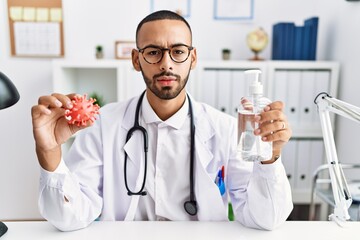 African american doctor man holding virus toy an sanitizer gel skeptic and nervous, frowning upset because of problem. negative person.