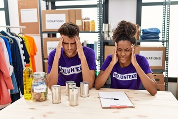 Young interracial people wearing volunteer t shirt at donations stand with hand on head for pain in...