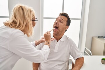 Obraz premium Middle age man and woman doctor and patient examining throat having medical consultation at clinic