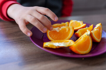 the boy is holding a slice of orange. A plate of sliced orange. 