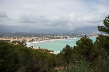 Detail of the coastline of Albir, in the municipality of Alfaz del Pi, with tall buildings next to the beach. Cloudy day and turquoise Mediterranean sea with waves.