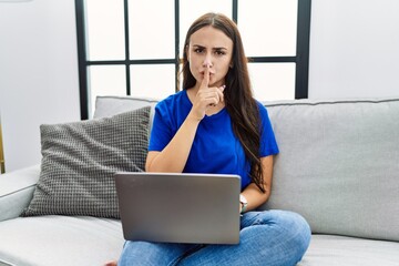 Fototapeta na wymiar Young brunette woman using laptop at home asking to be quiet with finger on lips. silence and secret concept.