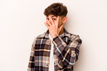 Young hispanic man isolated on white background blink at the camera through fingers, embarrassed covering face.
