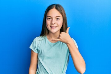 Beautiful brunette little girl wearing casual white t shirt smiling doing phone gesture with hand and fingers like talking on the telephone. communicating concepts.