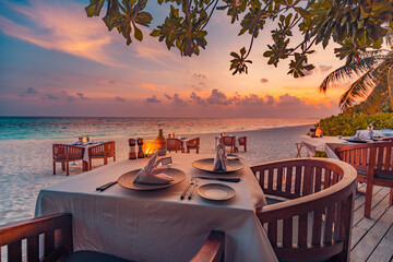 Romantic sunset on tropical island shore. Dinner table in beach restaurant. Beautiful sunset sky,...