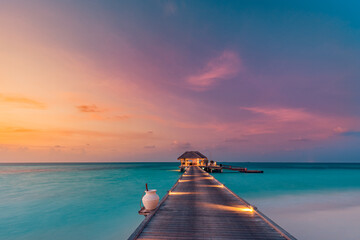Amazing sunset island landscape at Maldives. Luxury resort water villas jetty. Beautiful beach seascape with soft led lights colorful sky background for vacation holiday. Panoramic tropical paradise