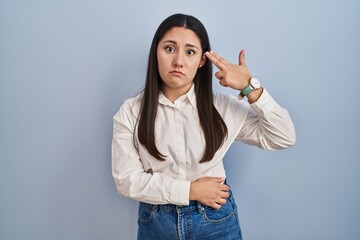 Young latin woman standing over blue background shooting and killing oneself pointing hand and fingers to head like gun, suicide gesture.