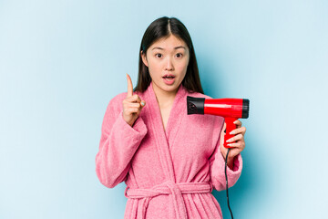 Young asian woman wearing a bathrobe and holding hairdryer isolated on pink background having some great idea, concept of creativity.