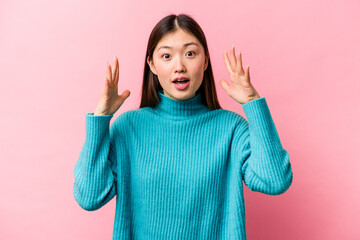 Young Chinese woman isolated on pink background celebrating a victory or success, he is surprised and shocked.