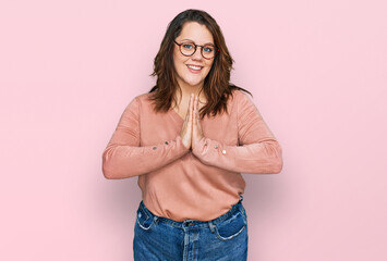 Young plus size woman wearing casual clothes and glasses praying with hands together asking for forgiveness smiling confident.