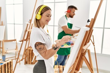 Young caucasian couple smiling happy listening to music and drawing at art studio.
