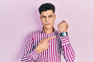 Fototapeta premium Young hispanic man wearing casual clothes in hurry pointing to watch time, impatience, looking at the camera with relaxed expression