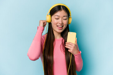 Young asian woman listening to music isolated on blue background