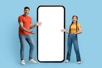 Mobile Offer. Excited Middle Eastern Couple Standing Near Big Blank Cellphone