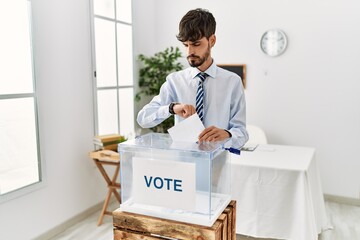 Hispanic man with beard voting putting envelop in ballot box checking the time on wrist watch,...
