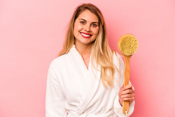 Young caucasian woman holding back scratcher isolated on pink background happy, smiling and cheerful.