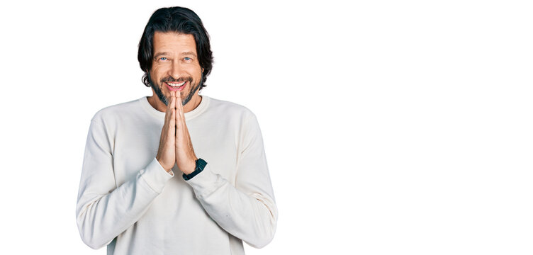 Middle age caucasian man wearing casual clothes praying with hands together asking for forgiveness smiling confident.