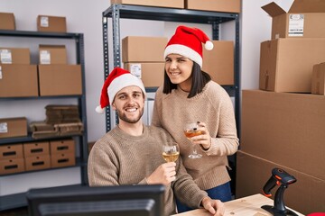 Man and woman ecommerce business workers wearing christmas hat toasting with champagne at office
