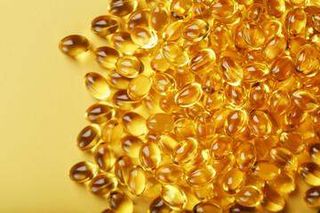 Heap of transparent fish oil capsules on yellow background with free space