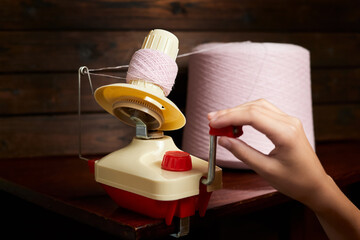 The girl rotates mechanical yarn winder or reel while rewinding thread. Close-up, selective focus