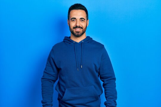 Handsome hispanic man with beard wearing casual sweatshirt with a happy and cool smile on face. lucky person.