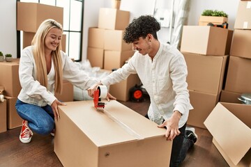 Young beautiful couple smiling happy packing cardboard box at new home.