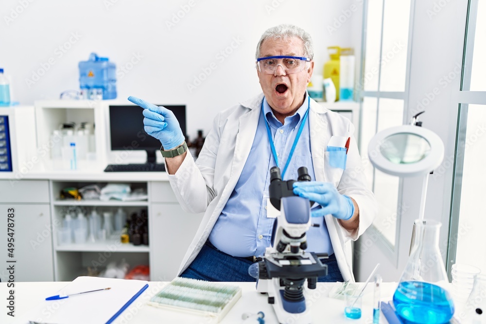 Canvas Prints Senior caucasian man working at scientist laboratory surprised pointing with finger to the side, open mouth amazed expression.