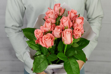 a bouquet of 11 coral pink roses in a white package in the hands of a man without a face