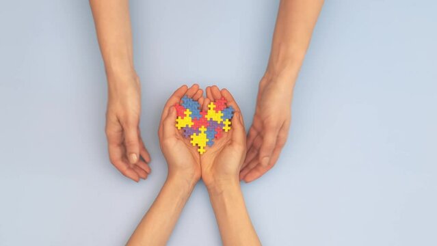 World autism awareness day concept. Woman and child hands holding puzzle heart on light blue background. Top view