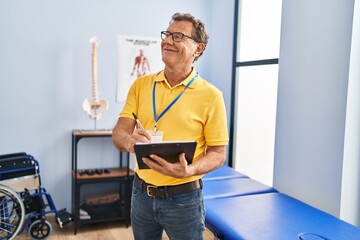 Middle age man physiotherapist writing on clipboard at physiotherpy clinic