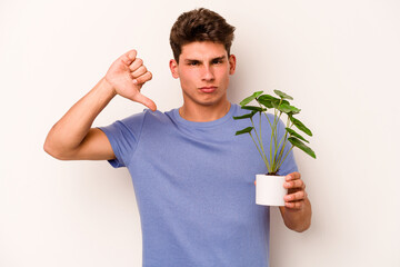 Young caucasian man holding a plant isolated on white background showing a dislike gesture, thumbs...
