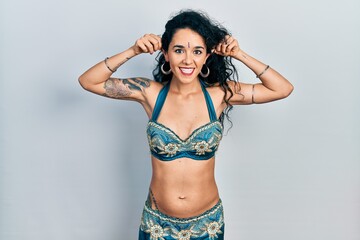 Young woman wearing bindi and traditional belly dance clothes smiling pulling ears with fingers, funny gesture. audition problem