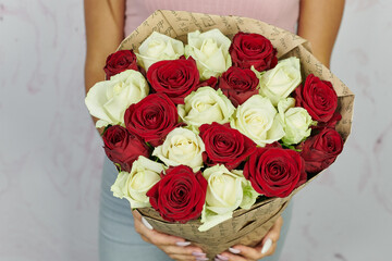 a bouquet of red and white roses with open buds in a brown kraft paper package in the hands of a girl without a face on a light background
