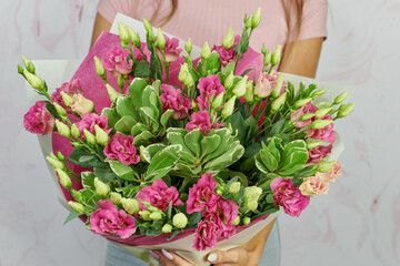 a bouquet of pink carnations with green leaves in a pink package in the hands of a girl without a face on a light background