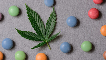 Cannabis leaf with colorful candy confetti close up. Marijuana sweets with CBD and THC on gray .background. Top view, flat lay.