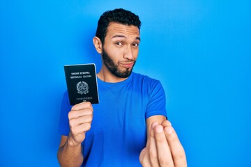 Hispanic man with beard holding italy passport doing money gesture with hands, asking for salary payment, millionaire business