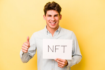 Young caucasian man holding NFT placard isolated on yellow background smiling and raising thumb up