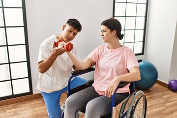 Young disabled woman sitting on wheelchair making mobility exercise using dumbbells at the clinic.
