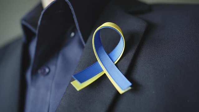 A man pins blue and yellow ribbon for Ukraine on the suit lapel