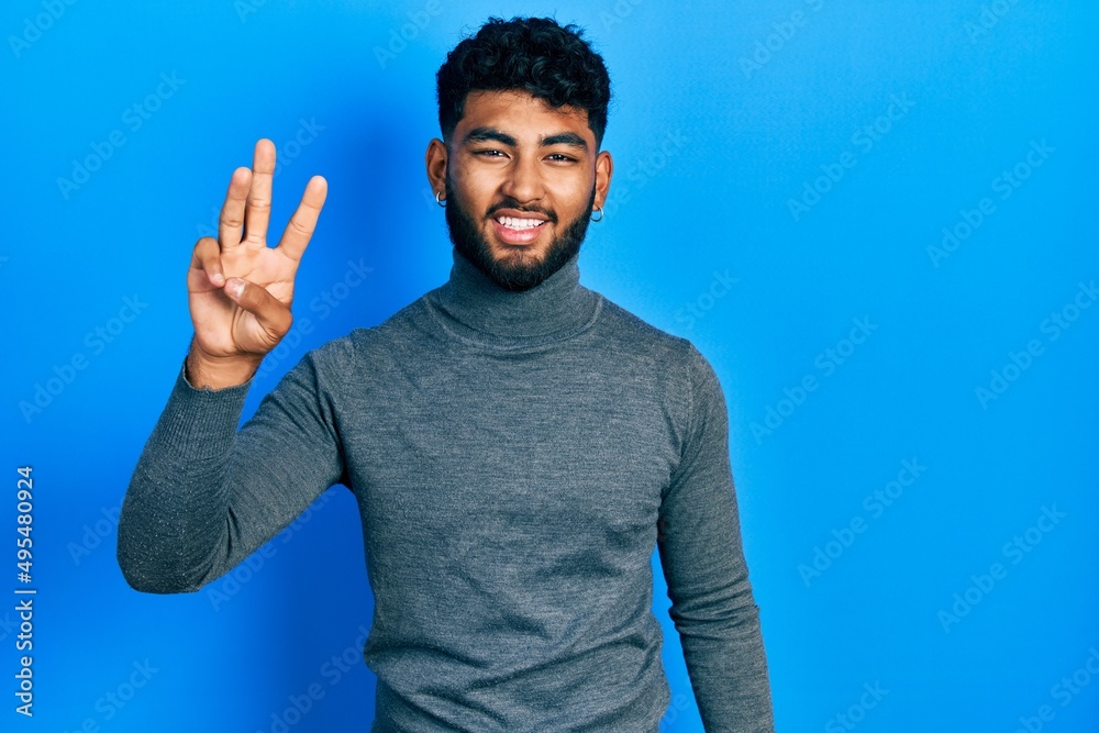 Canvas Prints Arab man with beard wearing turtleneck sweater showing and pointing up with fingers number three while smiling confident and happy.