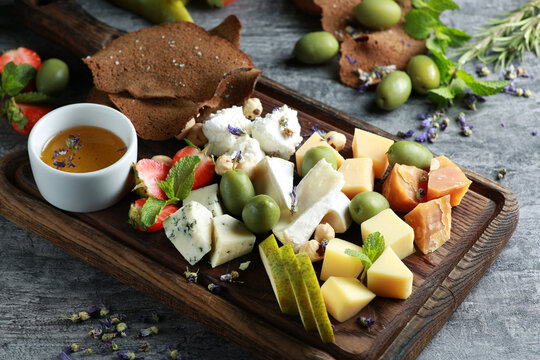 Cheese plate. Appetizer. Sliced hard cheese, cheese with mold, cheddar, camembert with olives, strawberries, pears, mint, nuts and croutons with bowl honey on dark wooden board. Background image
